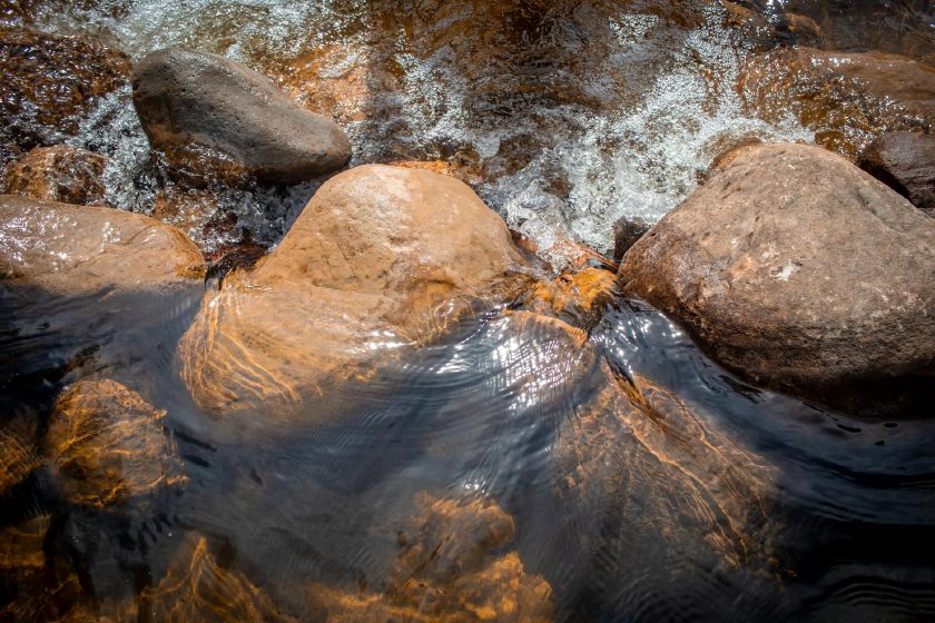 Ruhig fließendes Wasser über glatten Steinen in einem stillen Bachlauf