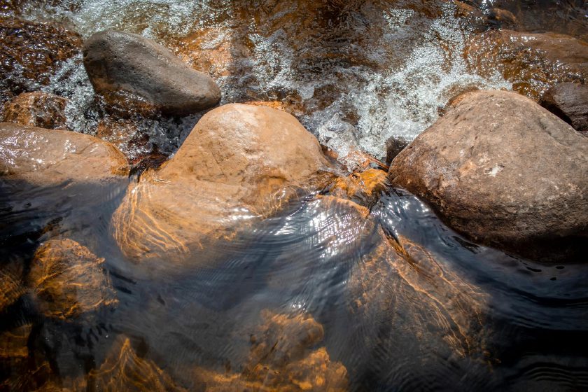 Ruhig fließendes Wasser über glatten Steinen in einem stillen Bachlauf