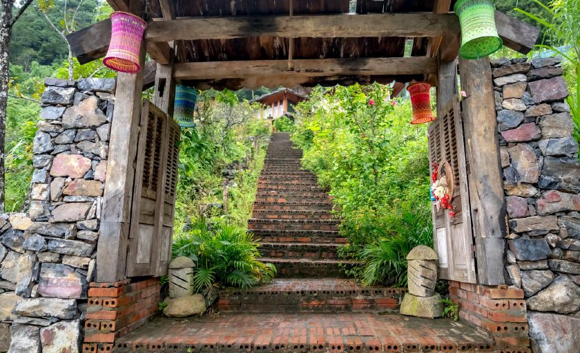 Rustikales Steintor mit Laternen, das auf eine geschwungene Steintreppe zu einem Rückzugsort auf einer Anhöhe führt
