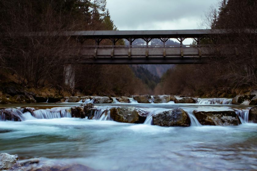 Rustikale Holzbrücke über einen ruhigen Fluss, eingebettet in eine natürliche Landschaft
